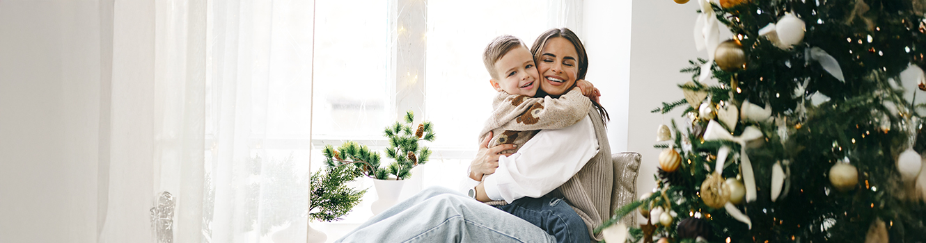 Happy mother with son sit on windowsill near Christmas tree